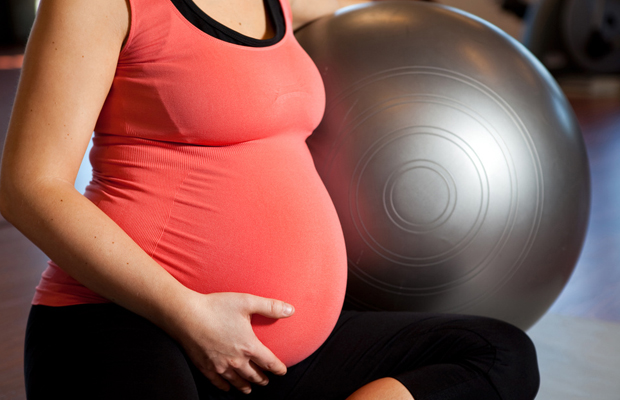A young pregnant woman doing relaxation exercise using a fitness ball and holding her tummy